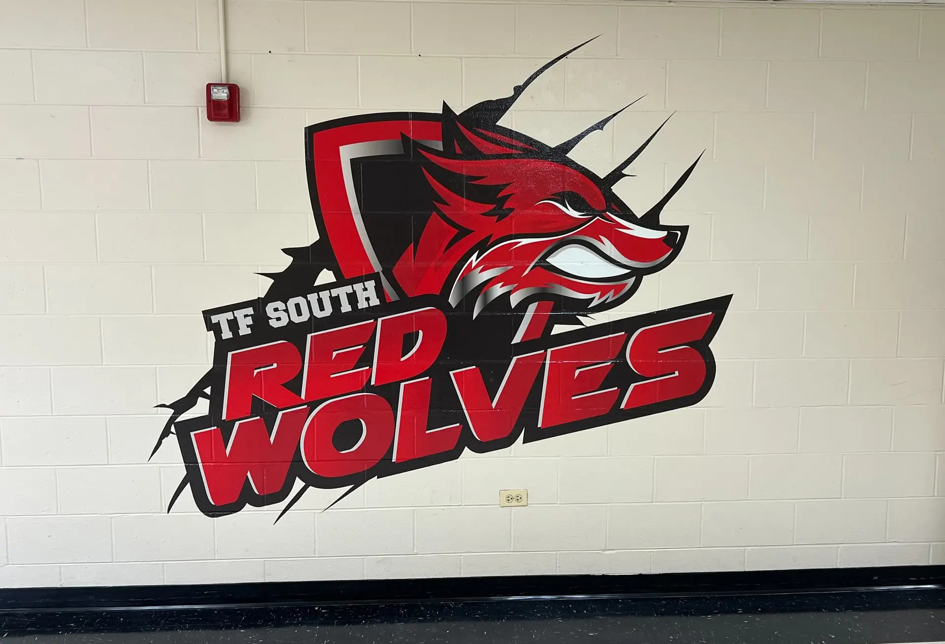 TF South Red Wolves mascot logo on a white brick wall